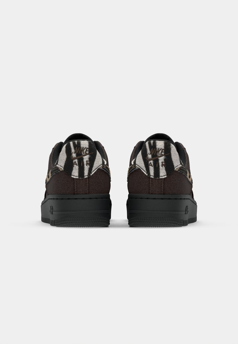 Braune Sneaker mit schwarzen Akzenten, ausgestattet mit einem strukturierten Obermaterial und einer dicken schwarzen Sohle. Hinten zeigt sich ein grafisches Design in Weiß und Schwarz.