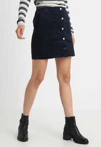 Marinblå kordkjol med framknäppning, lapplommer och en figursydd design. Kombinerad med svarta anklboots för kontrast.