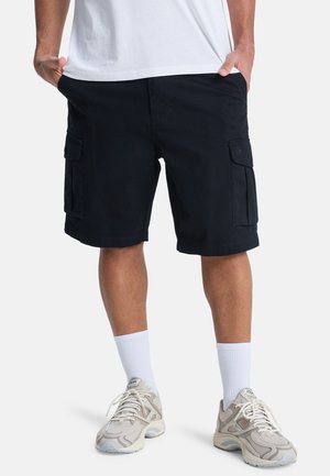 Pantaloncini cargo neri da uomo in cotone con due tasche laterali, vestibilità comoda e orlo piatto. Indossati con sneakers grigio chiaro e calzini bianchi.