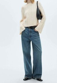 Pull en maille torsadée crème avec des manches larges, associé à un jean en denim bleu ample et des chaussures en cuir verni noir. Sac à main noir en accent.