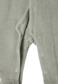 Grüner Cord-Overall mit Druckknöpfen entlang der Vorderseite und an den Innenbeinen, weicher Textur und einem dezenten Rippdesign.