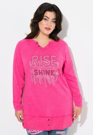 Langærmet pink top med V-hals, udsmykket "RISE SHINE" tekst i rhinsten og en rundet kant med knapdetalje nederst.