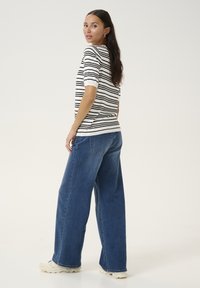 Haut à manches courtes rayé en blanc et noir, associé à un jeans en denim bleu à jambes larges. Le modèle se tient de profil, mettant en valeur l'ajustement de l'ensemble.