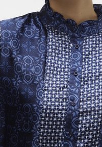 Camicia blu navy con fantasie miste: un lato con motivi floreali, l'altro con disegni geometrici. Collo arricciato e chiusura con bottoni frontali.