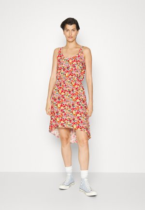 Vestido floral com cintura ajustada, decote em forma de barco e barra assimétrica. As cores incluem vermelho, rosa, amarelo e verde. Combinado com ténis azuis.