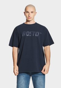 Granatowa bawełniana koszulka z wyrazistym, tonalnym logo "PROSTO" na klatce piersiowej. Luźny krój, krótkie rękawy i okrągły dekolt.