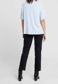 Ljusblå kortärmad topp i ett mjukt tyg, paret med svarta raka jeans med fransade fångar, bärs med svarta klackstövlar.