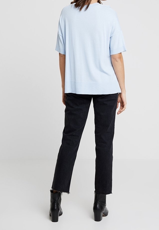 Ljusblå kortärmad topp i ett mjukt tyg, paret med svarta raka jeans med fransade fångar, bärs med svarta klackstövlar.