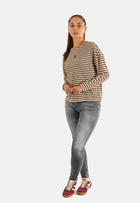 Maglione a maniche lunghe a righe marroni e crema, abbinato a jeans blu sbiaditi e sneaker rosse con dettagli bianchi. Design semplice e vestibilità casual.