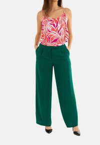 Top senza maniche a righe rosa e bianche abbinato a pantaloni larghi verdi. Tessuto morbido, vestibilità rilassata e tasche laterali nei pantaloni.