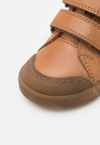 Bruine leren schoen met dubbele klittenbandsluitingen, ronde neus, gestructureerd oppervlak en een contrasterende rubberen zool met stikseldetails.