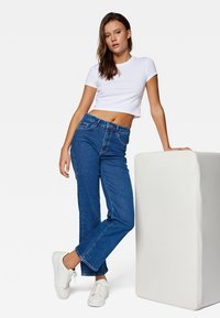 Blue denim jeans with a high waist, straight leg, and five pockets paired with a fitted white crop top and white sneakers.