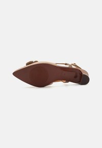 Chaussure à talon hauteur marron avec un bout pointu, semelle texturée et sangle réglable. Matériau supérieur lisse et marquage circulaire distinct sur la semelle.