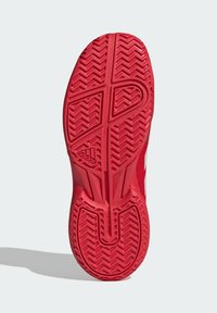 Röd gummisula till sneakers med ett distinkt fiskbensmönster, med strukturerad yta för grepp och med varumärkeslogotyp nära hälen.
