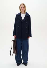 Pardosea de marină cu design cu două rânduri de nasturi, nasturi mari; combinată cu pantaloni din denim albastru oversized și o geantă tote din piele maro.