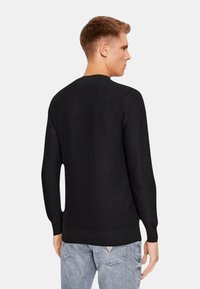 Maglione nero con una trama liscia, scollo rotondo e maniche lunghe. Presenta polsini e orlo a costine, mostrato da dietro.