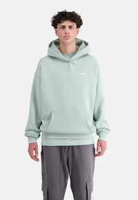 Mintgrüner Hoodie aus weichigem Stoff, mit einer vorderen Tasche und verstellbarem Kapuzenschild, sowie einem kleinen weißen Logo auf der Brust.