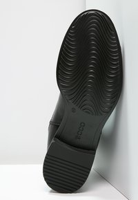 Black leather shoe with a textured rubber sole featuring curved grooves and ridges. Brand logo visible on the sole's surface.