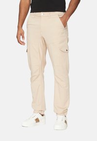 Pantalones cargo beige con un diseño ajustado, bolsillos laterales y una textura suave, combinados con zapatillas blancas con acentos marrones.