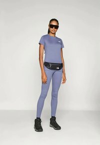 Tricou sportiv mov și colanți, asociați cu un rucsac mic negru și bocanci de drumeție negri. Ochelarii de soare completează ținuta.