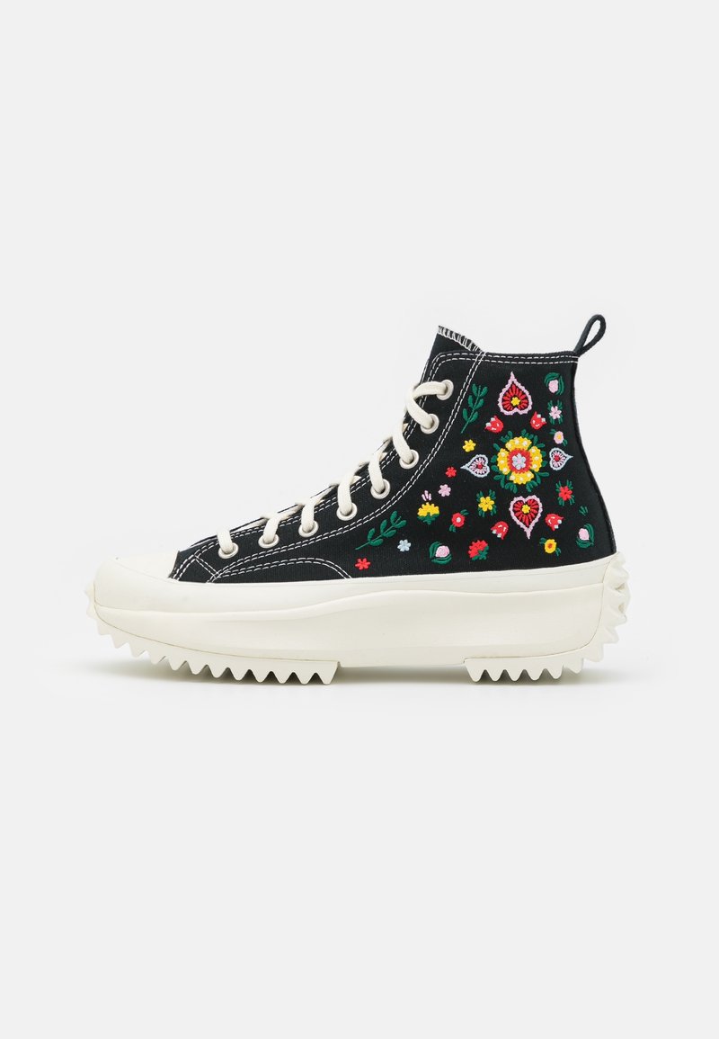 High-top black canvas sneakers with colorful floral embroidery, white rubber sole, and jagged edges. Features white laces and a pull tab.
