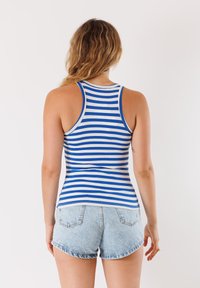 Canotta a righe blu e bianche con un design attillato, abbinata a pantaloncini in denim chiaro. Il tessuto appare liscio con una vestibilità elasticizzata.