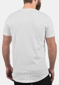 Weißes T-Shirt mit kurzen Ärmeln und einem schwarzen Punkte-Muster. Mit Rundhalsausschnitt und regulärer Passform. Glatte, baumwollähnliche Textur.