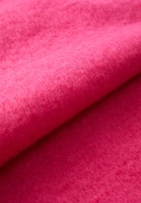 Filtstof i levende pink med en blød, tekstureret overflade. Materialet virker tykt og varmt og viser en ensartet farve uden mønstre.