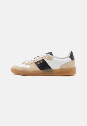 Sneaker sportive con tomaia in pelle bianca, dettagli in suede beige, striscia nera laterale e suola in gomma naturale. Design con lacci e dettaglio del logo.