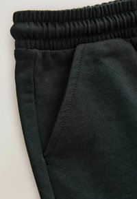 Mustad puuvillased püksid, millel on elastne vöökoht, küljetaskud ja sile, tekstureeritud viimistlus. Õmblused on nähtavad mööda õmblusi.