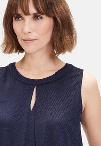Marineblaue ärmellose Bluse aus strukturiertem Stoff mit leichtem Glanz, mit einem Schlüsselloch-Detail am Ausschnitt und einem glatten Kragen.