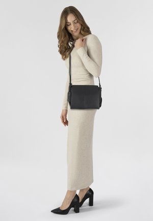 Bolso cruzado de piel negra con correa ajustable, forma rectangular y diseño minimalista; presenta un detalle de etiqueta y acabado texturizado.