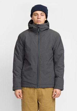 Gray insulated jacket with a high collar, full zip, and hood. Features elastic cuffs and side pockets. Worn with a navy knit beanie.