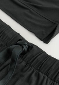 Abbigliamento sportivo nero esposto, con una vita annodata sui pantaloni shorts e una maglietta liscia, su uno sfondo chiaro, mettendo in risalto la texture e il design.