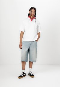 Hvid kortærmet skjorte, lyseblå denimshorts til knæene og sorte sneakers med hvide detaljer. Et rødt bandana bundet om halsen.