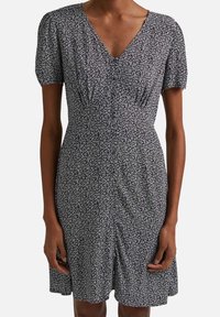 Schwarzes und weißes Blumenkleid mit kurzen Puffärmeln, V-Ausschnitt, tailliertem Bund und gerafften Details entlang des Rocks.