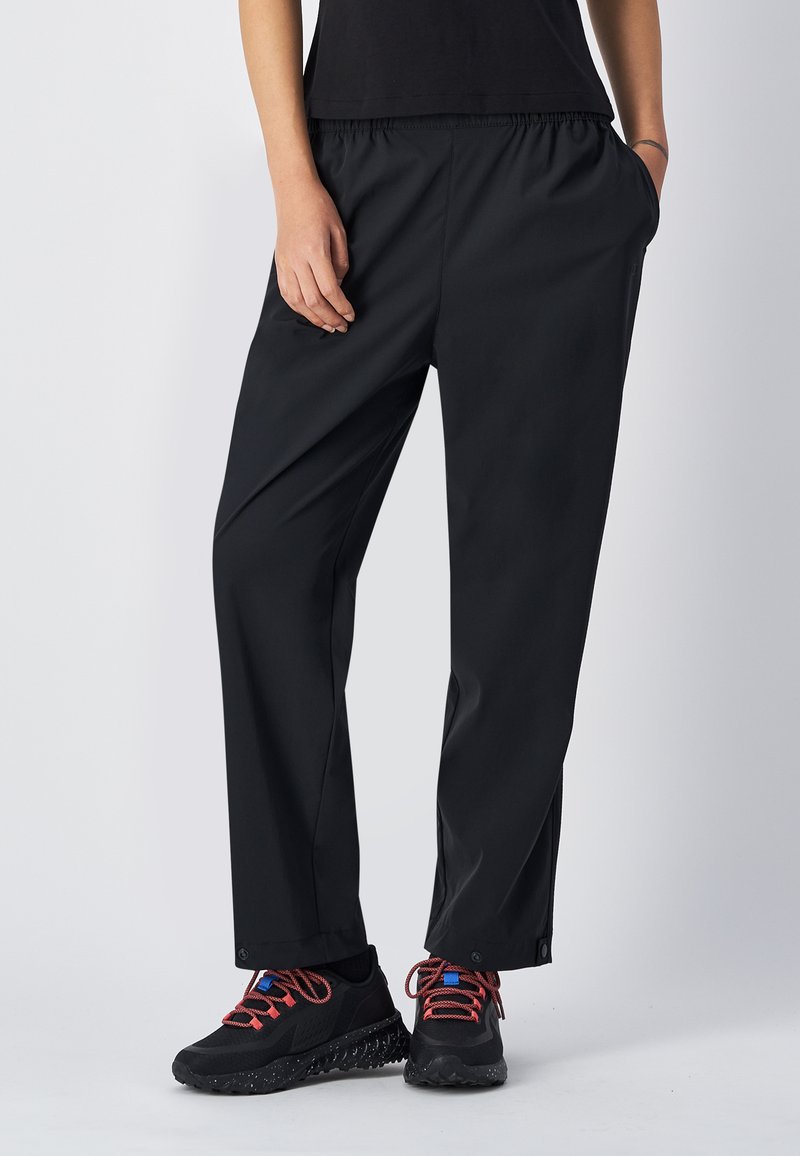 Zwarte waterdichte broek met een elastische tailleband, zijzakken en een losse pasvorm. Gecombineerd met zwarte sneakers met kleurrijke veters.