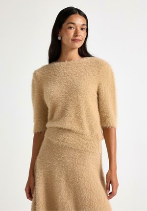 Beige, mjuk tröja med korta ärmar, med en vid halsringning och en strukturerad yta. Kombineras med en matchande kjol som framhävs.