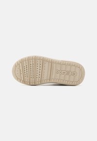 Suela de zapato de goma beige con patrones de agarre texturizados, perforaciones circulares y el logo de la marca "GEOX". Diseño plano con forma redondeada.