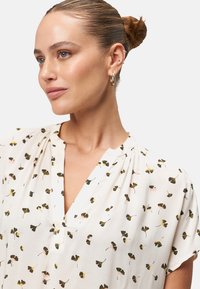 Witte blouse met een V-hals en korte mouwen, met een bloemmotief in groen, zwart en roze. Zachte stof met een relaxte pasvorm.
