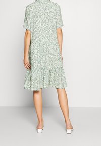 Abito verde a fiori con maniche corte, orlo a balze a livelli, tessuto leggero, motivo di margherite bianche e una vestibilità comoda.