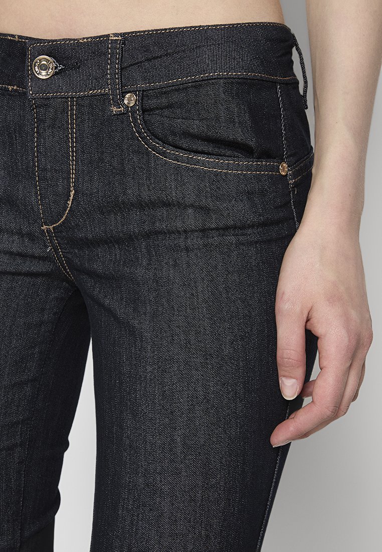 Jeans in denim blu scuro con un design aderente. Le caratteristiche includono un bottone anteriore, tasche classiche e cuciture evidenti in tonalità più chiare.