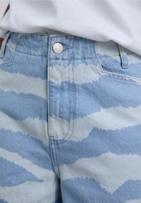 Light blue jeans with a wavy white stripe pattern. Features a metal button closure and classic five-pocket design. Denim texture visible.