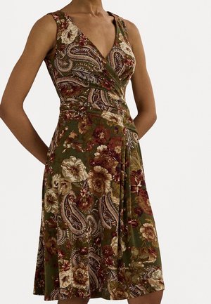 Mouwloze wikkeljurk met diepe V-hals in groene stof met grote bloemen- en paisleypatronen in bruine, crèmekleurige en bordeaux tinten.