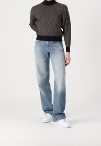 Pull noir à motifs avec un col montant, associé à un jean bleu clair à jambes droites et des baskets blanches. Tricot texturé et coupe décontractée.