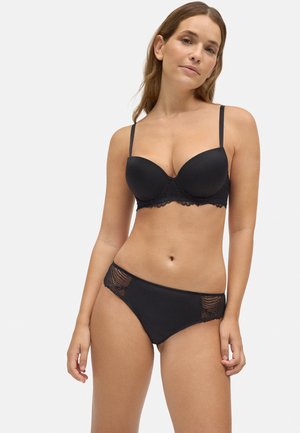 Sujeta de encaje negro con aros y tirantes ajustables, combinada con braguitas a juego que presentan acentos de encaje en los laterales.