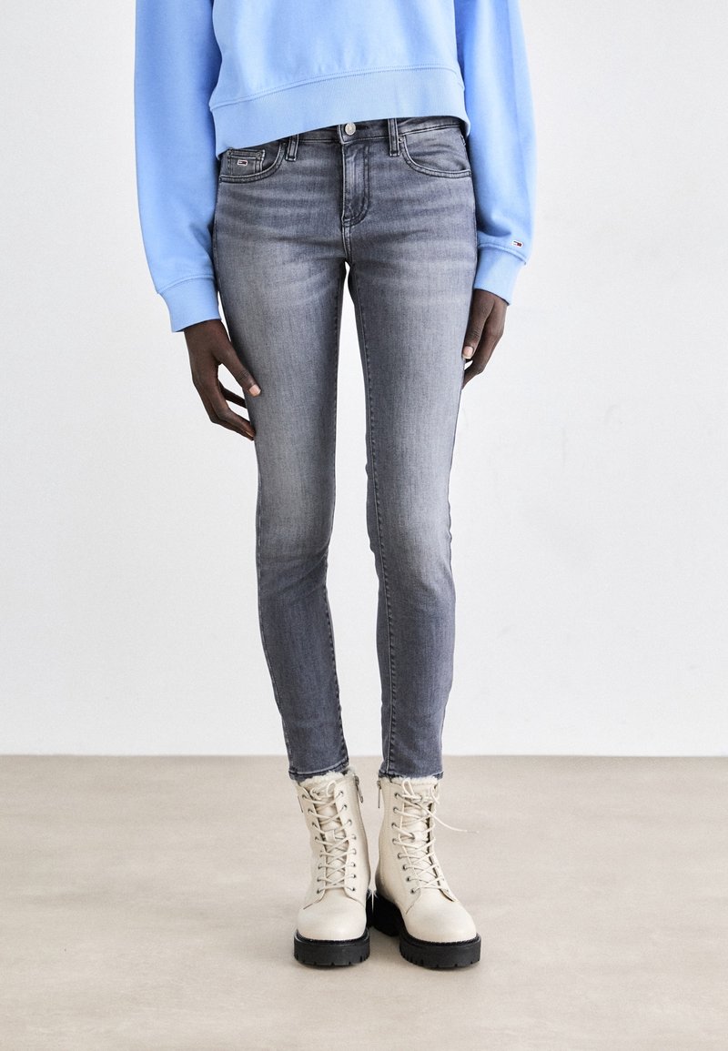 Jeans skinny grises con un lavado desgastado, combinados con botas militares beiges con cordones y un sudadera azul clara. Tela de mezclilla suave y elástica.