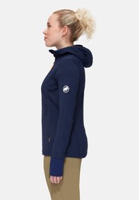 Navy zip-up jacket with hood, ribbed texture, orange accents, and logo patch on sleeve. Features thumbholes at cuffs for added comfort.