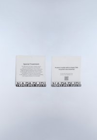 Kaksi etikettiä, joissa on valkoinen tausta ja musta teksti. Sana "NAPAPIJRI" näkyy lihavoituna pohjassa. Yhdessä etiketeistä kerrotaan erityiskohtelusta; toisessa mainitaan 70 % kierrätetystä materiaalista.