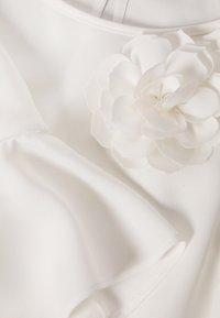 Biały top z tkaniny z kwiatową aplikacją, gładką fakturą, okrągłym dekoltem i lekko bufiaste rękawy.